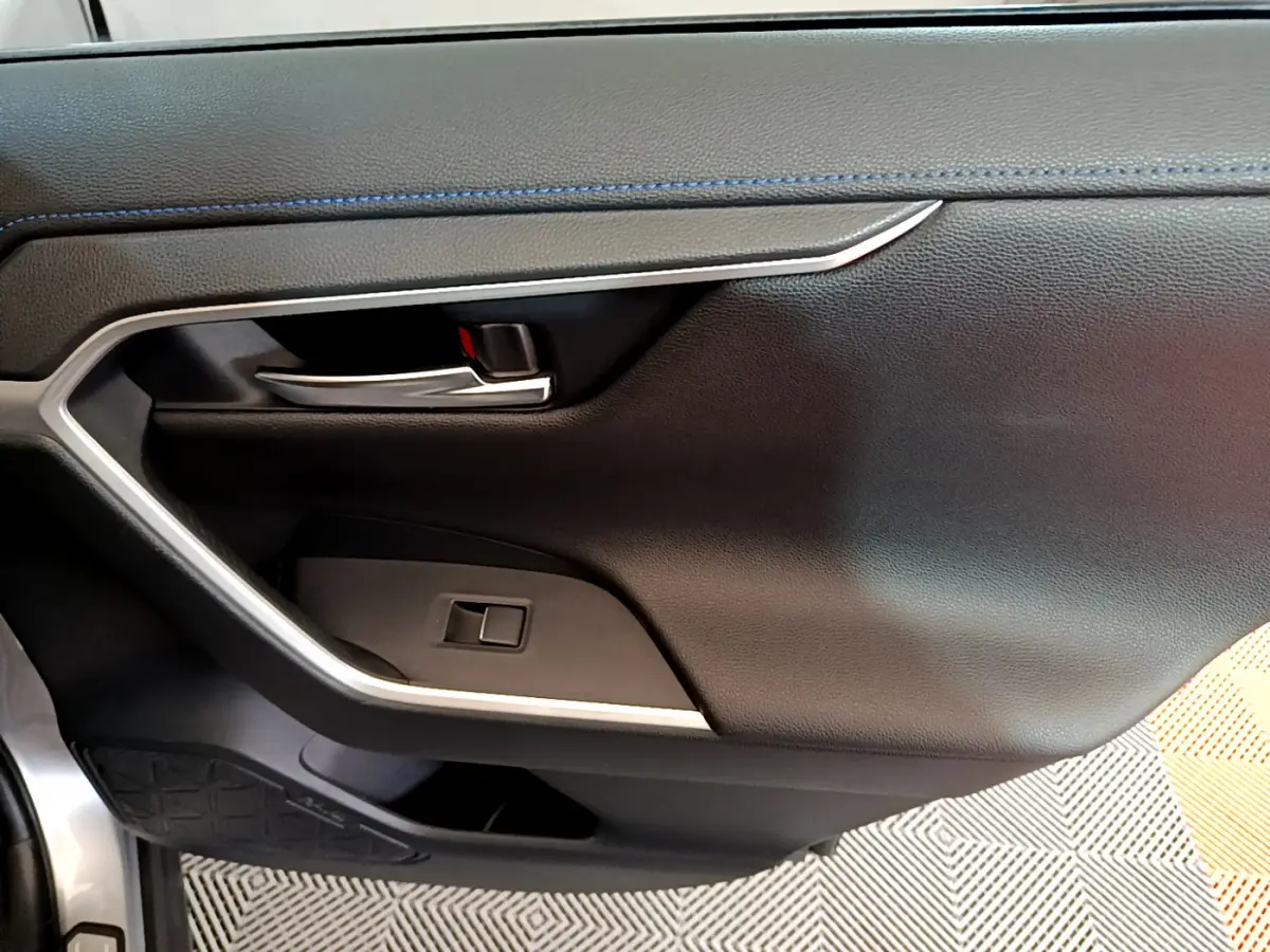 Détail de la porte intérieure côté gauche du Toyota RAV4 gris clair avec poignée chrome et surpiqûres bleues.