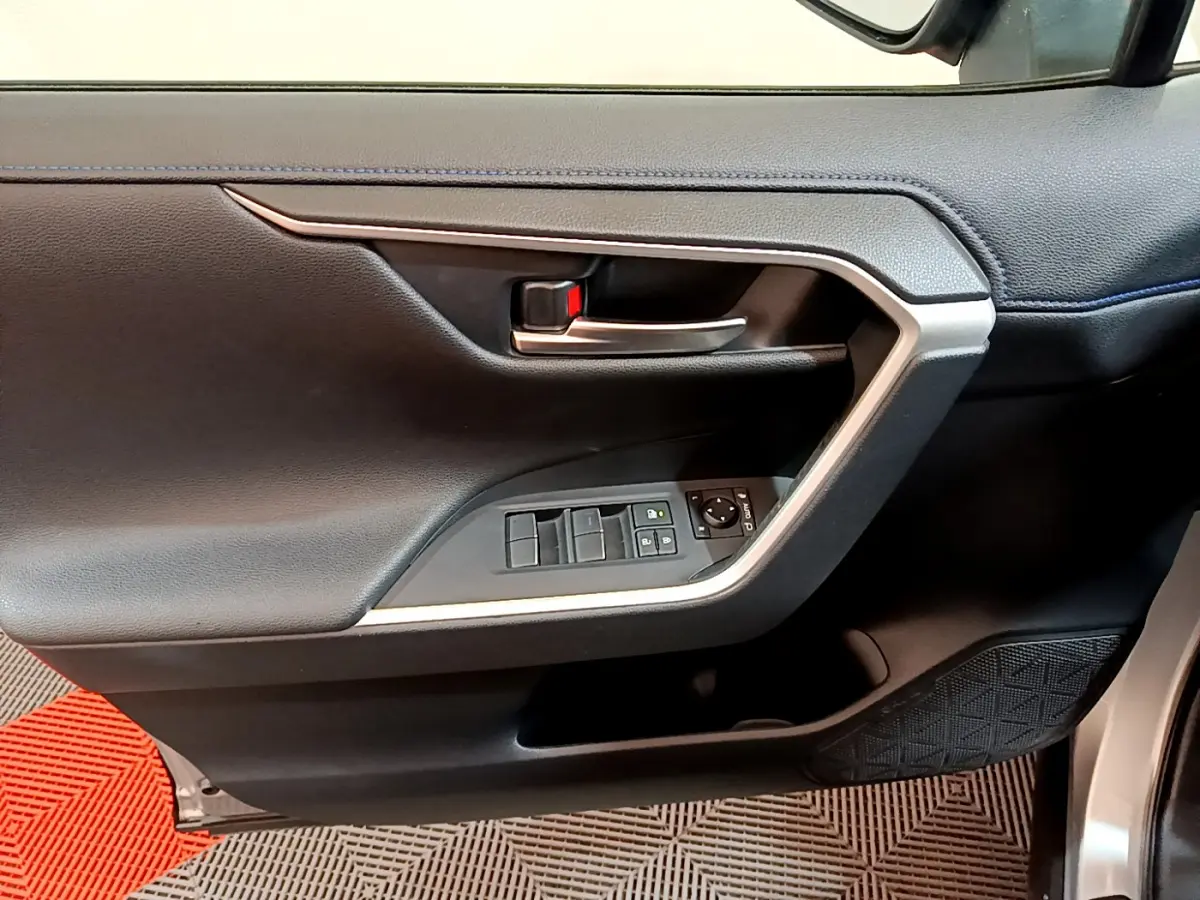 Gros plan sur la porte intérieure côté conducteur du Toyota RAV4 gris clair, avec commandes de vitres et poignée argentée.