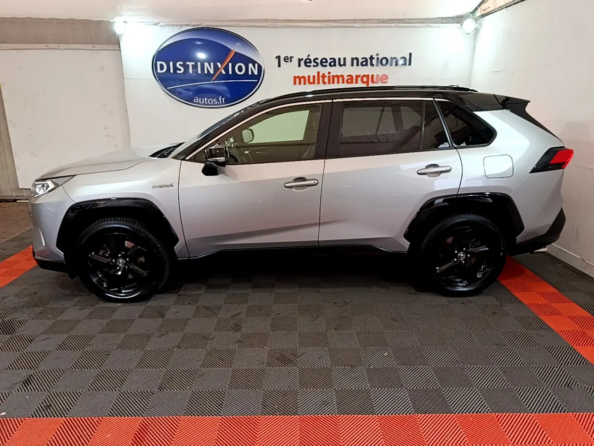 Profil côté gauche d'un Toyota RAV4 gris clair 2WD 218ch Collection avec jantes noires en intérieur showroom.
