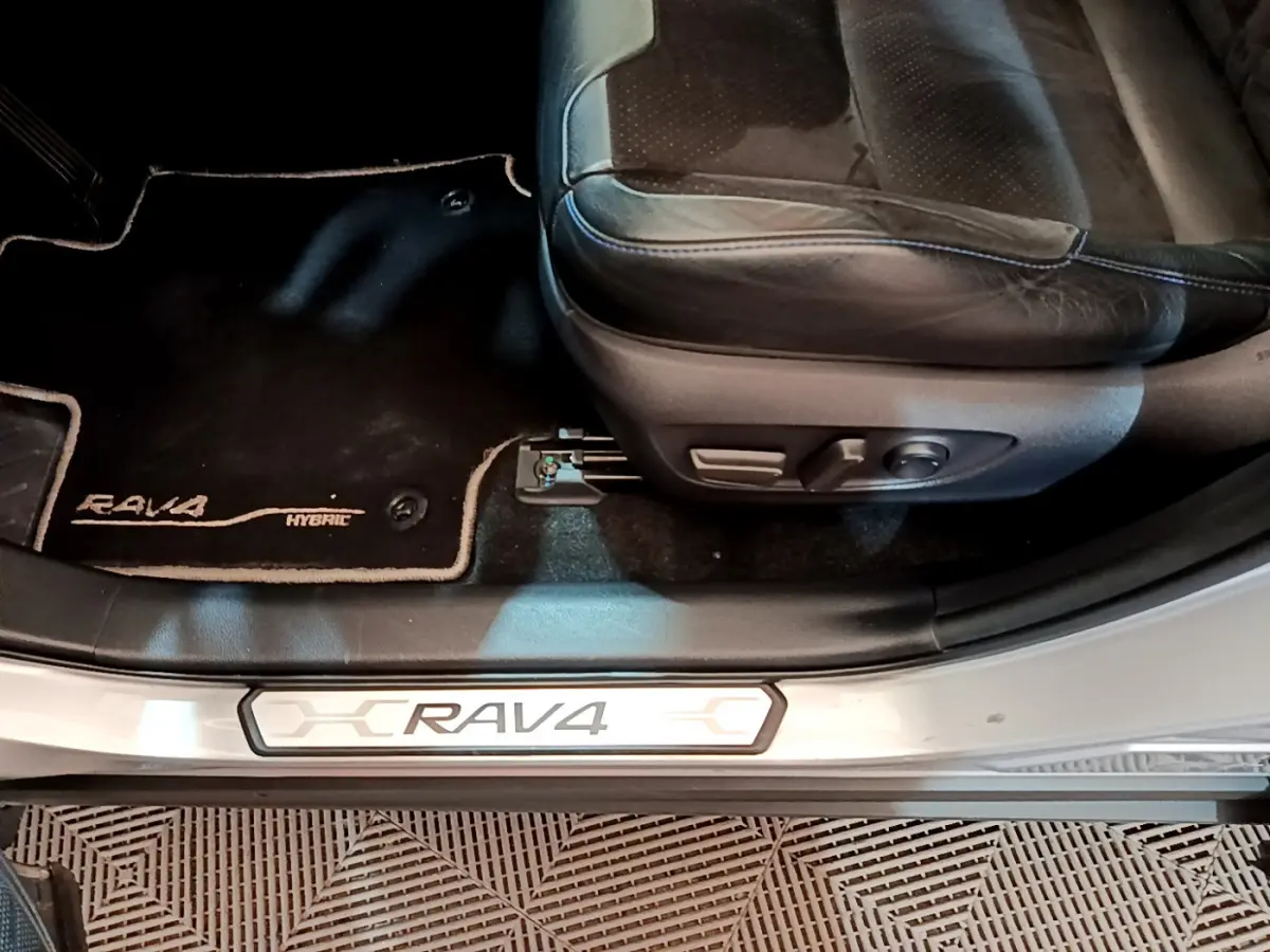 Détail intérieur côté conducteur du Toyota RAV4 gris clair, montrant siège en cuir et tapis avec logo Hybrid.