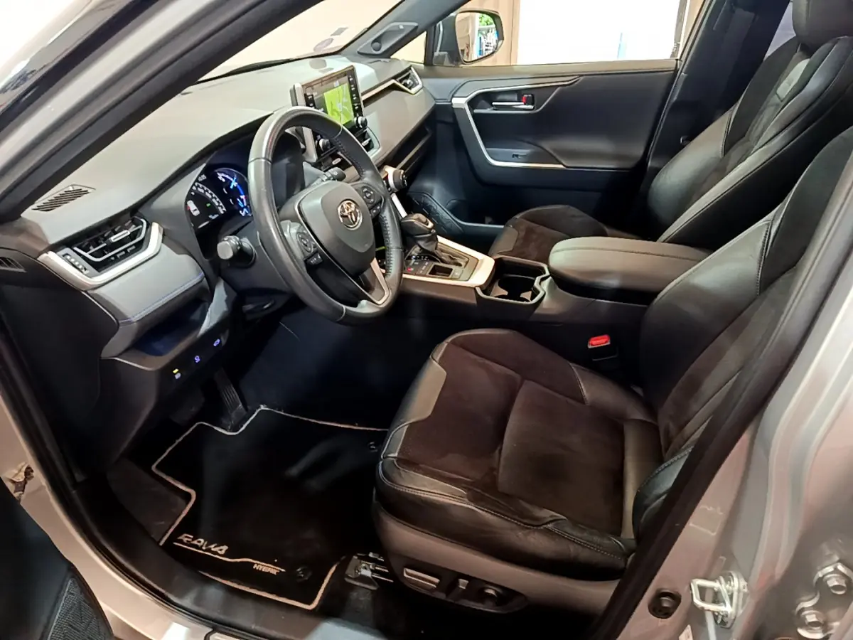 Intérieur du Toyota RAV4 gris clair vu côté conducteur, sièges cuir noir et tableau de bord moderne avec écran tactile.