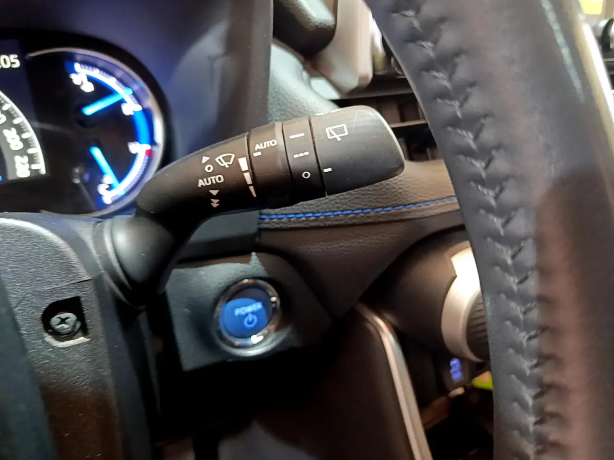 Gros plan intérieur sur la manette d'essuie-glace et bouton start bleu du Toyota RAV4 gris clair 2019 côté gauche du volant.