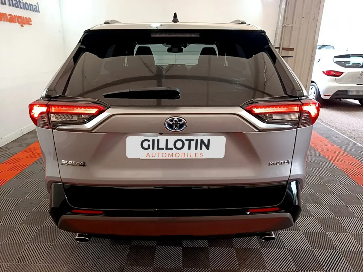 Vue arrière du Toyota RAV4 gris clair hybride avec feux LED allumés et logo visible sur un sol à damiers rouge et noir.