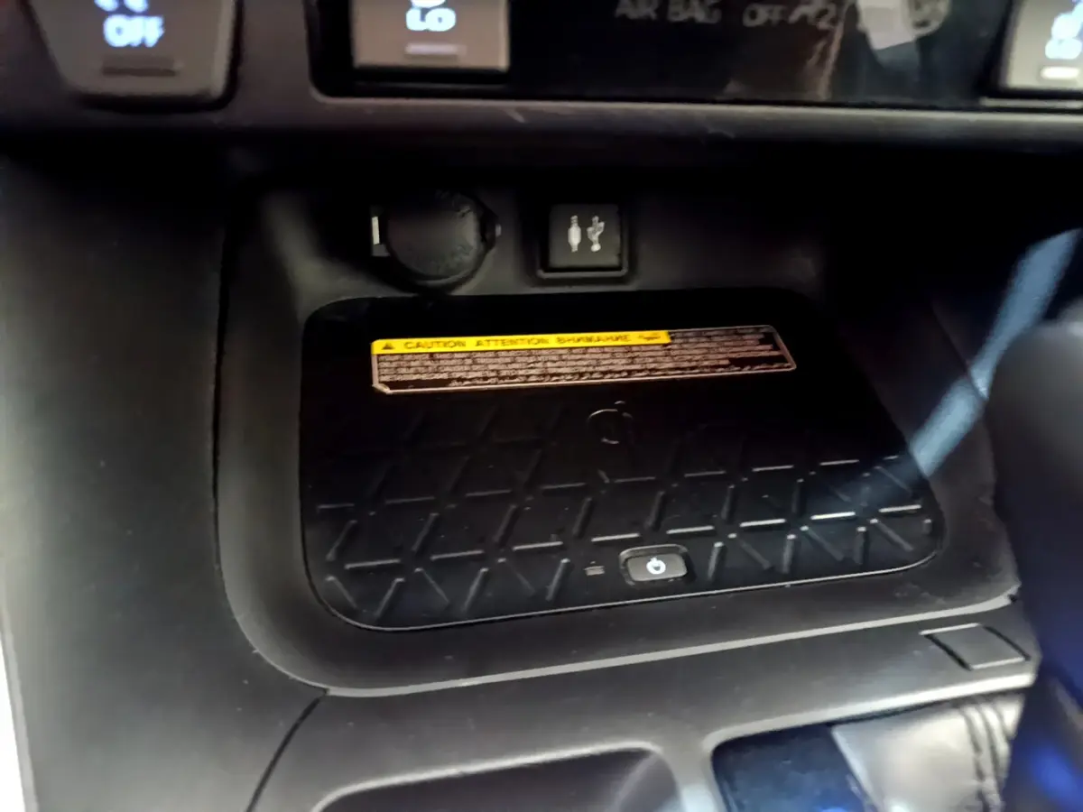 Gros plan sur la zone de recharge sans fil noire du Toyota RAV4 gris clair, avec prise USB et bouton tactile visible.
