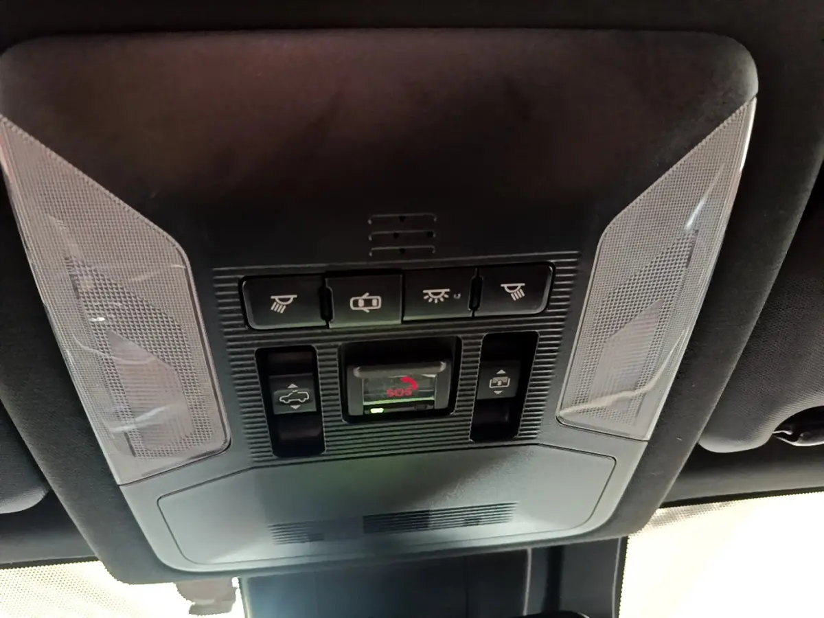 Vue en contre-plongée du panneau de commandes au plafond intérieur du Toyota RAV4 gris clair, avec bouton SOS et éclairages intégrés.