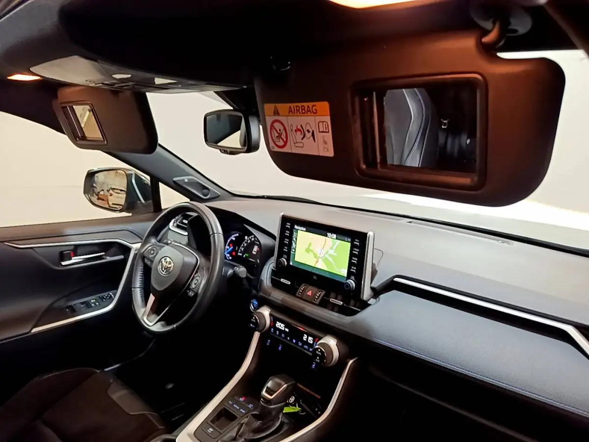 Intérieur du Toyota RAV4 2WD gris clair, vue côté conducteur, tableau de bord avec écran tactile et volant cuir.