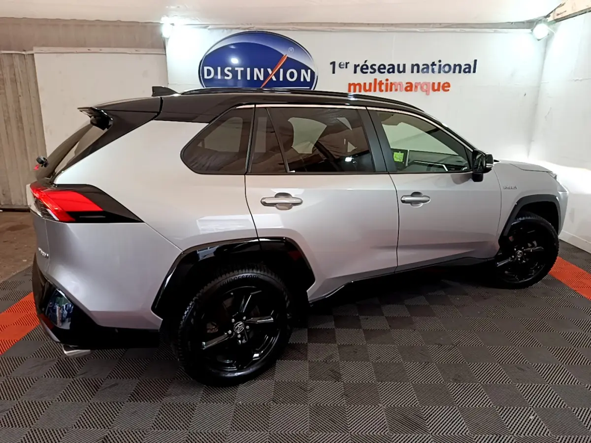 Vue de profil côté gauche d'un Toyota RAV4 2WD gris clair avec toit noir et jantes noires dans un showroom.