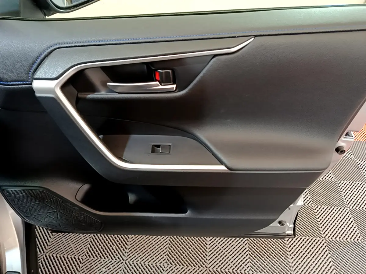 Gros plan sur la porte intérieure côté conducteur du Toyota RAV4 gris clair, avec poignée argentée et haut-parleur intégré.