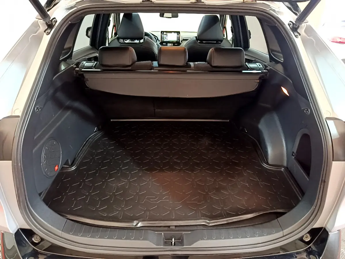 Coffre ouvert d'un Toyota RAV4 gris clair, vue arrière montrant la surface de chargement avec tapis caoutchouc marqué RAV4.
