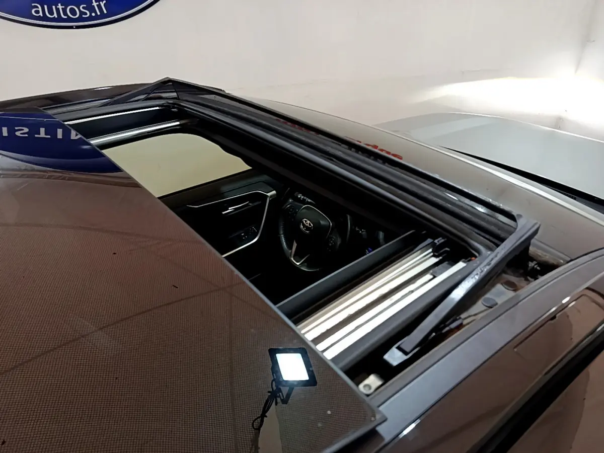 Toit ouvrant panoramique ouvert sur un Toyota RAV4 gris clair, vue plongeante sur l'intérieur côté conducteur.