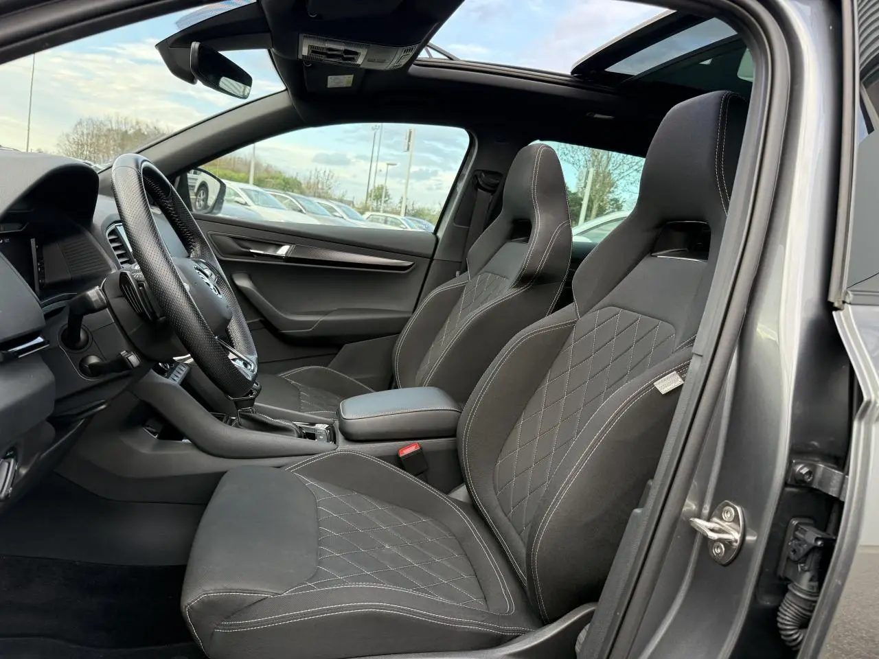 Intérieur avant du Skoda Karoq gris graphite, sièges sport noirs avec surpiqûres blanches et toit ouvrant panoramique en verre.