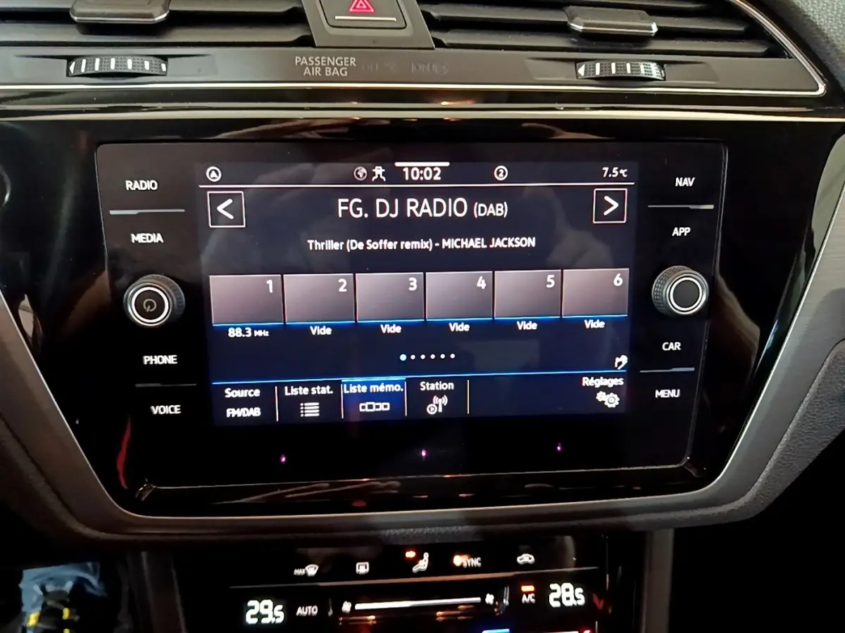 Écran tactile central du tableau de bord du Volkswagen Touran gris foncé, affichant la radio FM avec commandes autour.