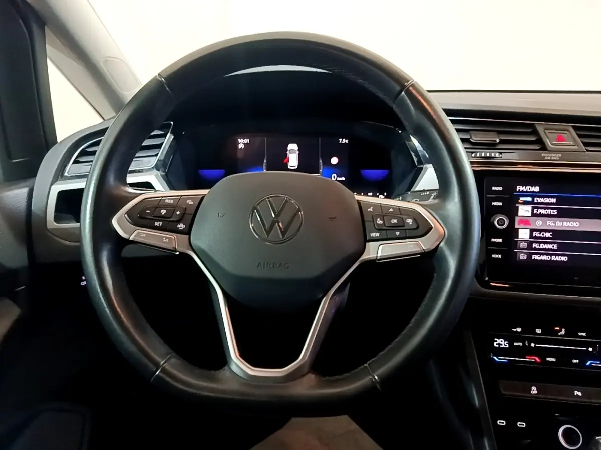 Vue intérieure centrée sur le volant cuir noir du Volkswagen Touran 2023 avec tableau de bord digital et écran tactile.