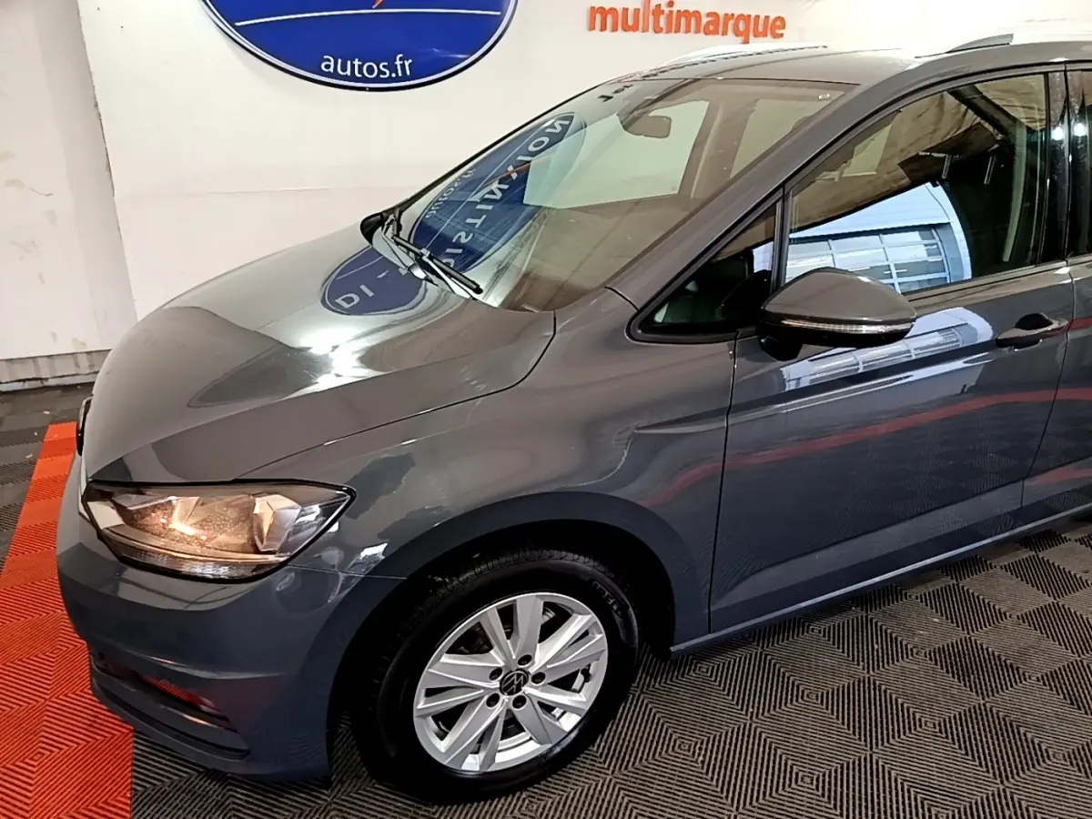 Vue 3/4 avant gauche d'un Volkswagen Touran gris foncé avec jantes alliage et rétroviseur assorti.