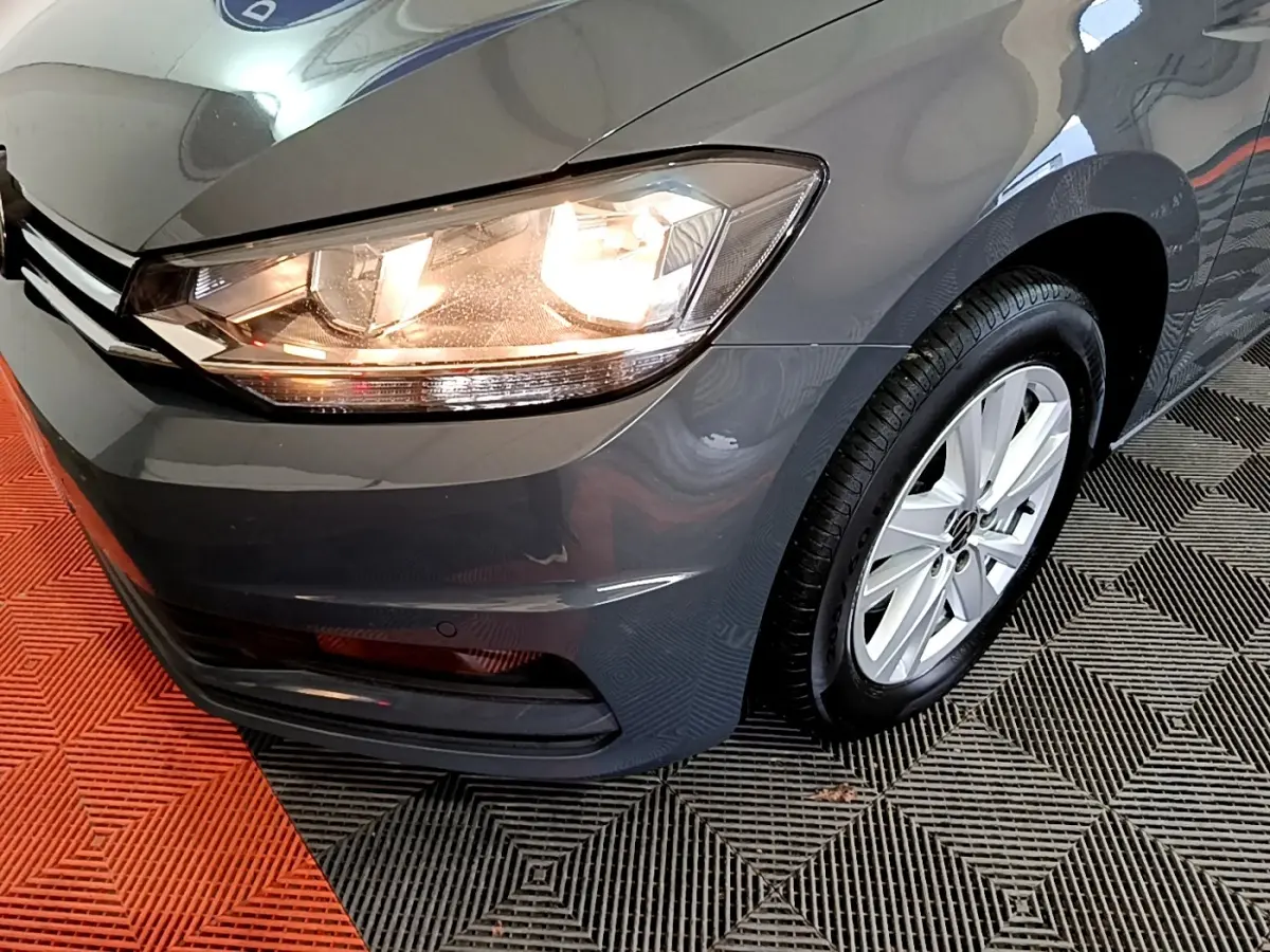 Gros plan sur l'avant droit gris foncé du Volkswagen Touran 2023 avec phare allumé et jante aluminium.