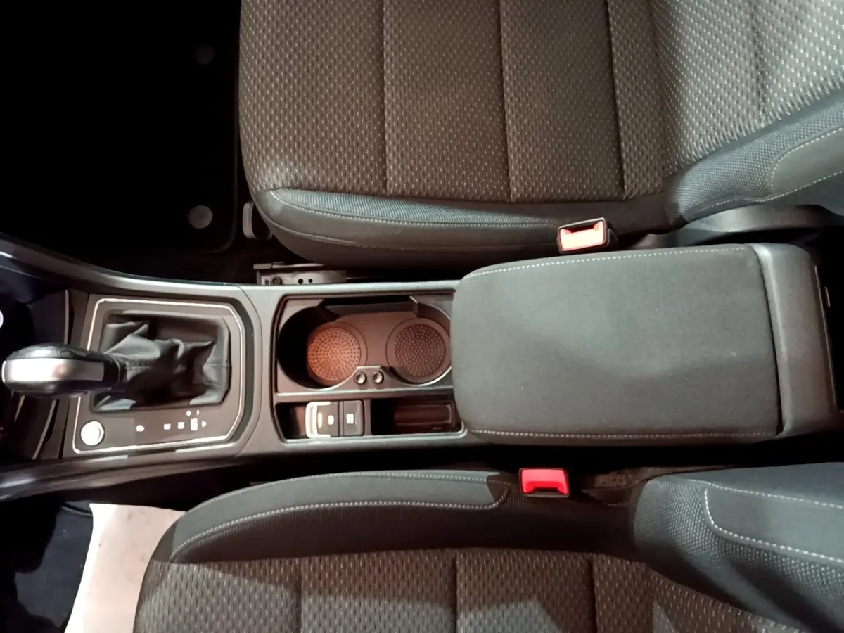 Vue plongeante sur la console centrale du Volkswagen Touran gris foncé, avec levier de vitesses automatique et accoudoir rembourré.