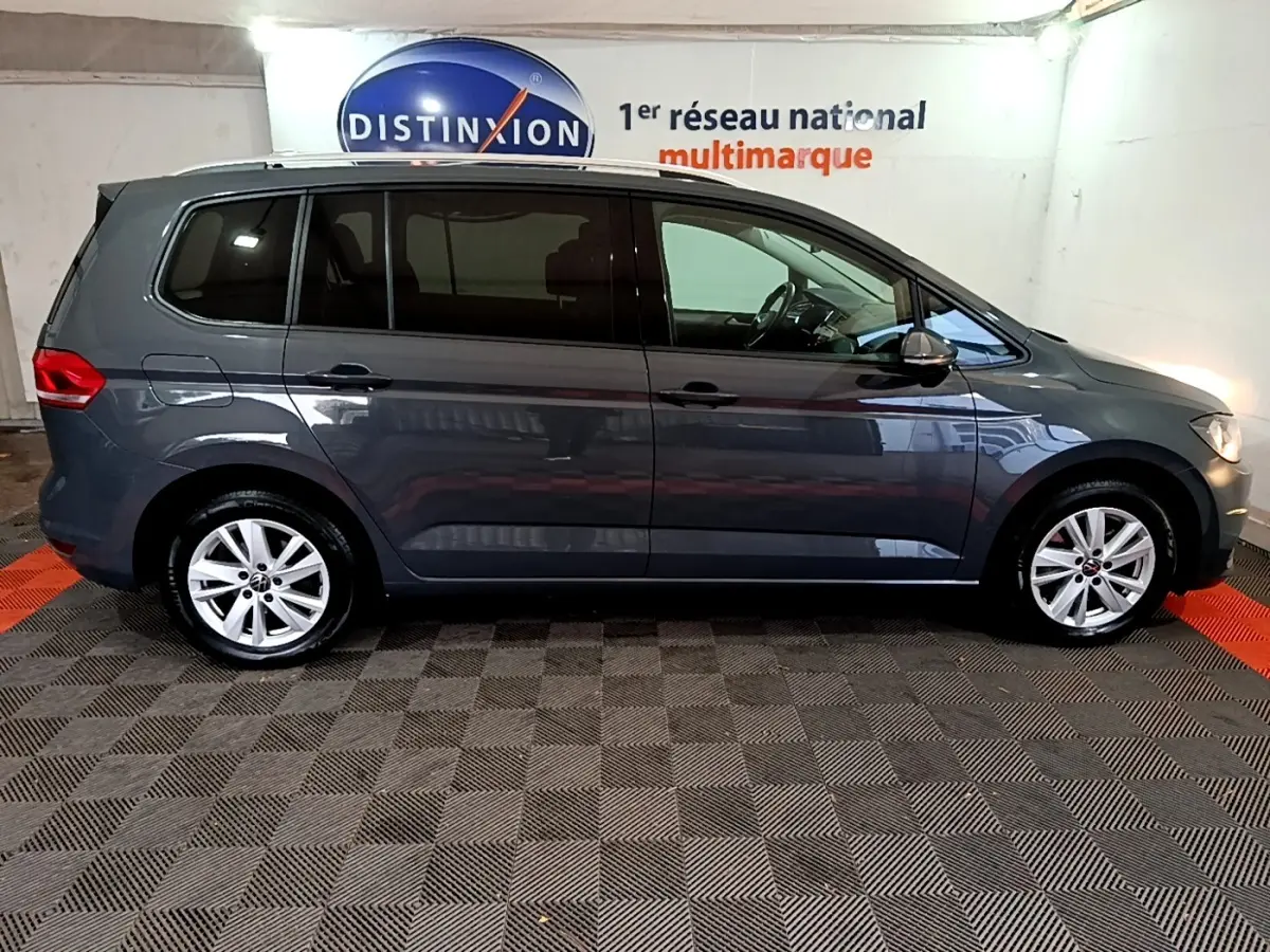 Profil droit d'un Volkswagen Touran gris foncé 2023 garé en intérieur avec jantes alliage et vitres teintées.