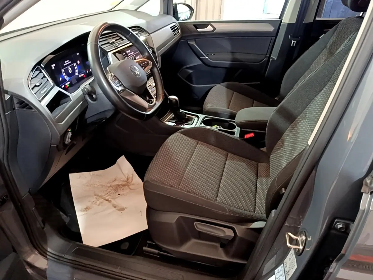 Vue intérieure côté conducteur du Volkswagen Touran gris foncé 2023, volant cuir et tableau de bord digital visible.