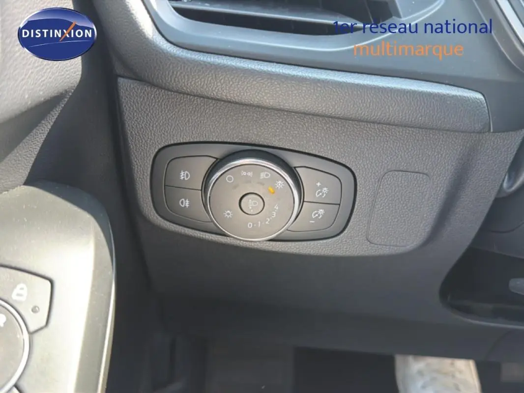 Gros plan sur la commande d’éclairage à gauche du volant dans l’habitacle sombre d’une Ford Focus SW bleu foncé 2022.