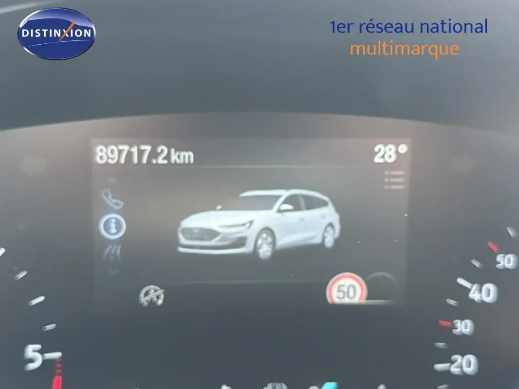 Affichage numérique du tableau de bord montrant une Ford Focus SW blanche en vue 3/4 avant, avec compteur et température.