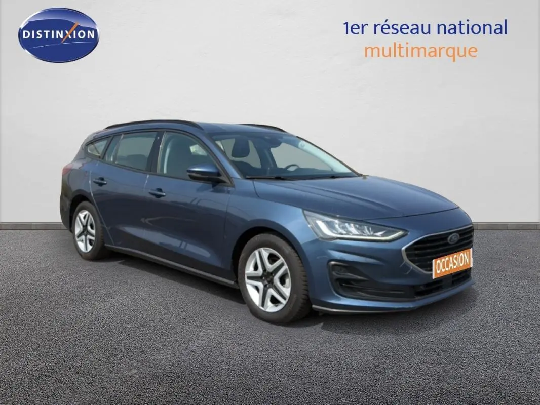 Ford Focus SW bleu foncé vue 3/4 avant droit, avec barres de toit et jantes classiques 16 pouces visibles.