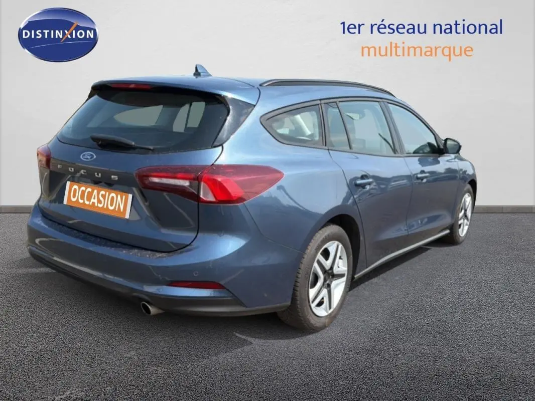 Vue 3/4 arrière droite d'une Ford Focus SW bleu foncé avec barres de toit et jantes classiques 16 pouces.