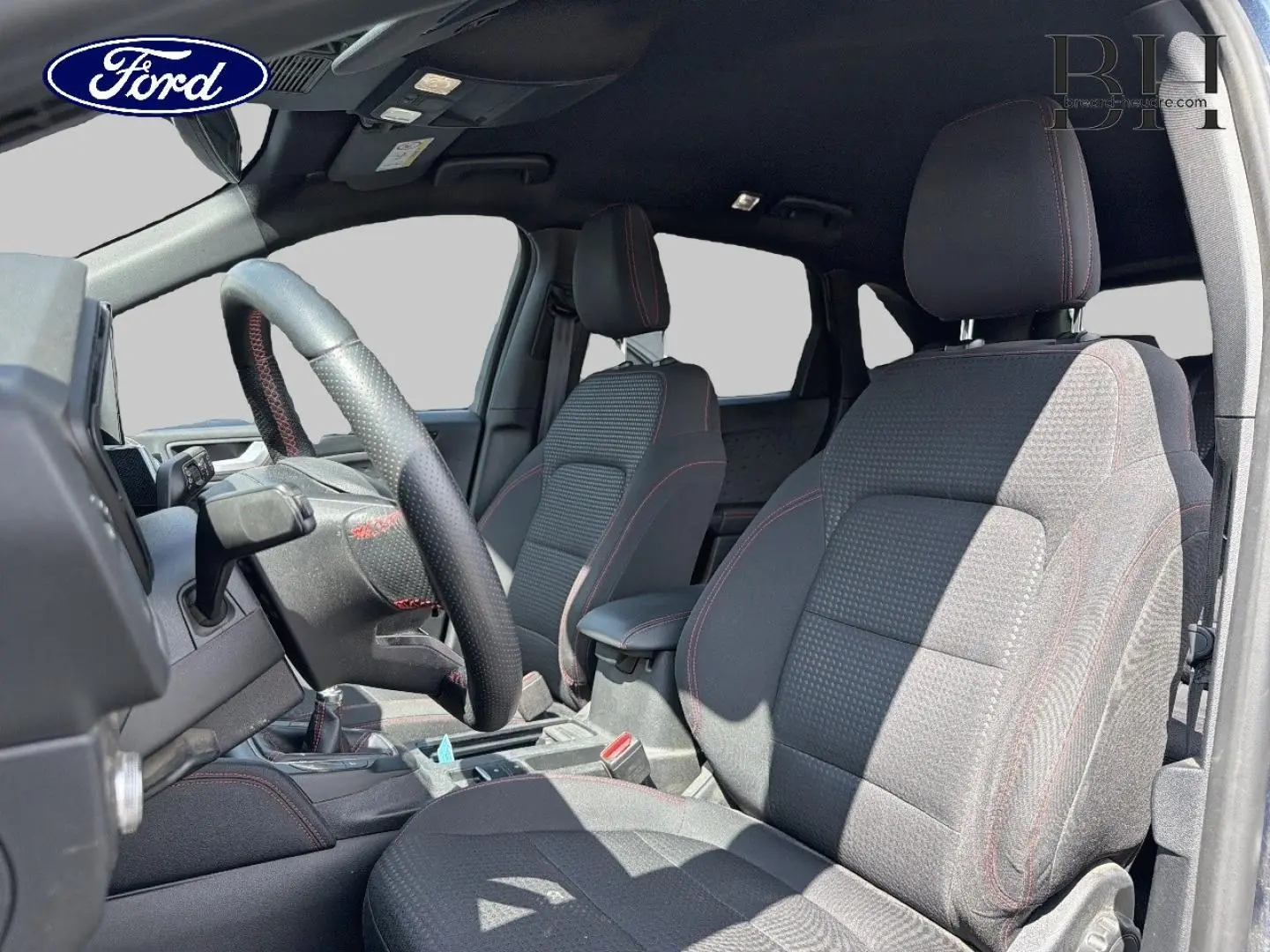 Vue intérieure côté conducteur du Ford Kuga 2020, sièges sport noirs avec surpiqûres rouges et volant cuir multifonction.