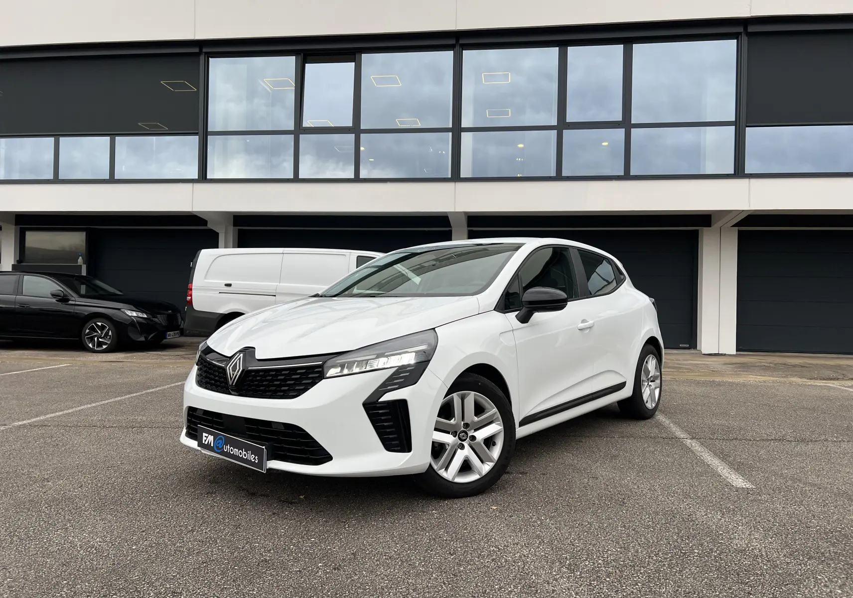 Renault Clio V blanche vue 3/4 avant droit, avec rétroviseurs noir perle et jantes 16 pouces.