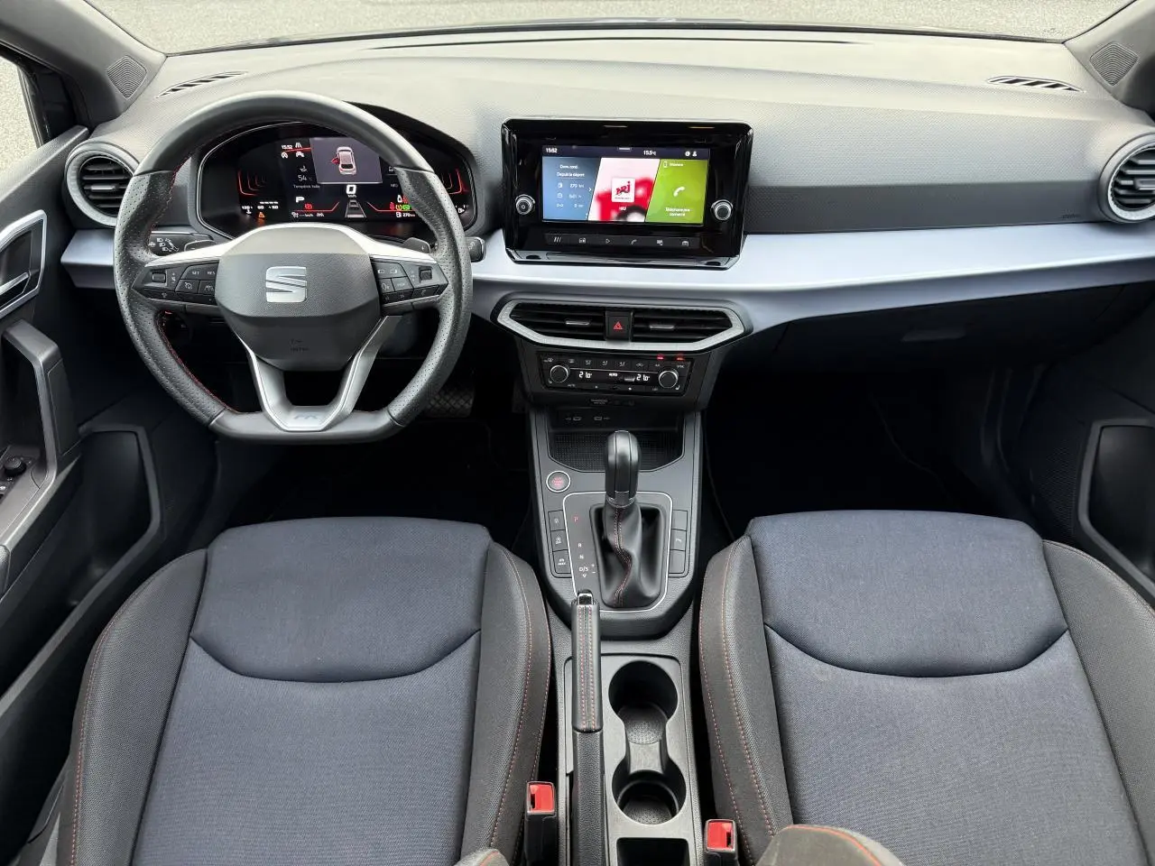 Vue intérieure frontale du tableau de bord et des sièges gris foncé d'une SEAT IBIZA 2024 avec volant multifonction et écran tactile central.
