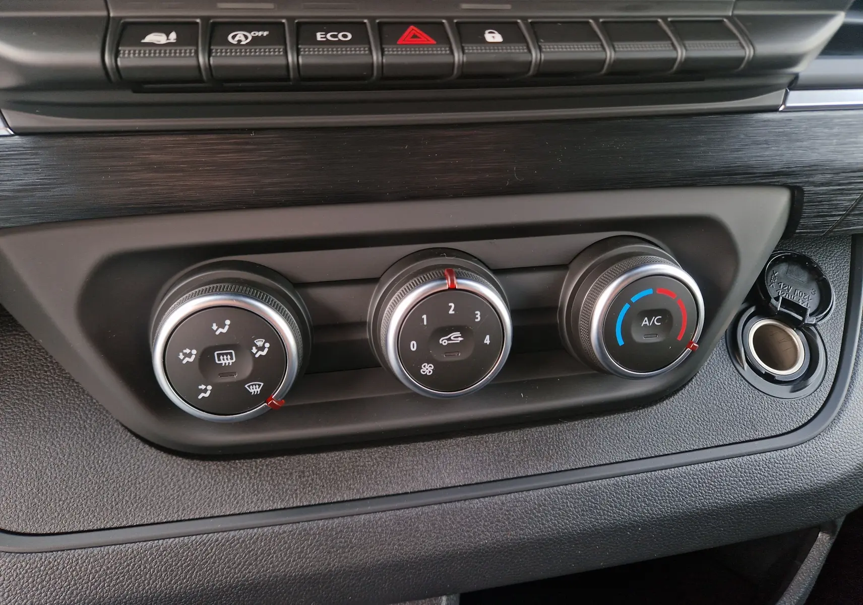Gros plan sur les commandes de climatisation du Nissan Primastar 2025, avec boutons rotatifs et prise 12V visible.
