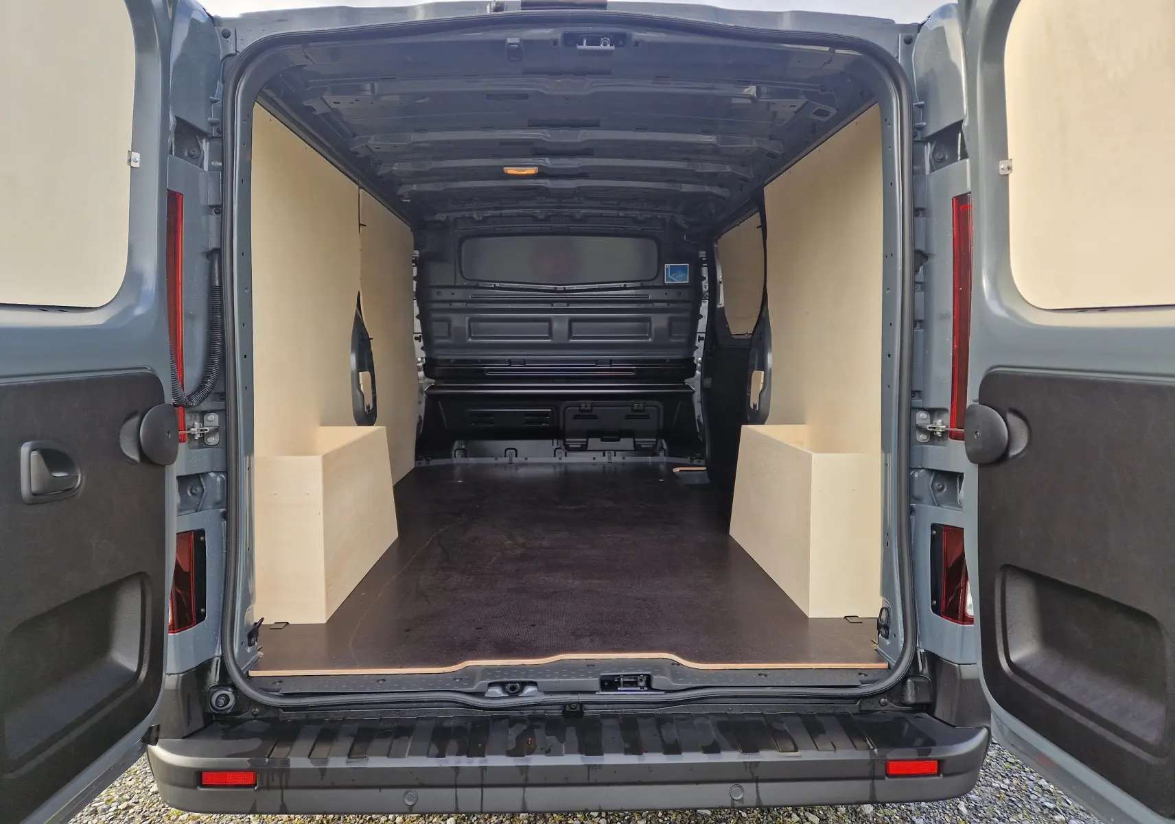 Vue arrière ouverte du Nissan Primastar gris urbain 2025, montrant l'intérieur spacieux avec aménagement bois Pack Cargo.