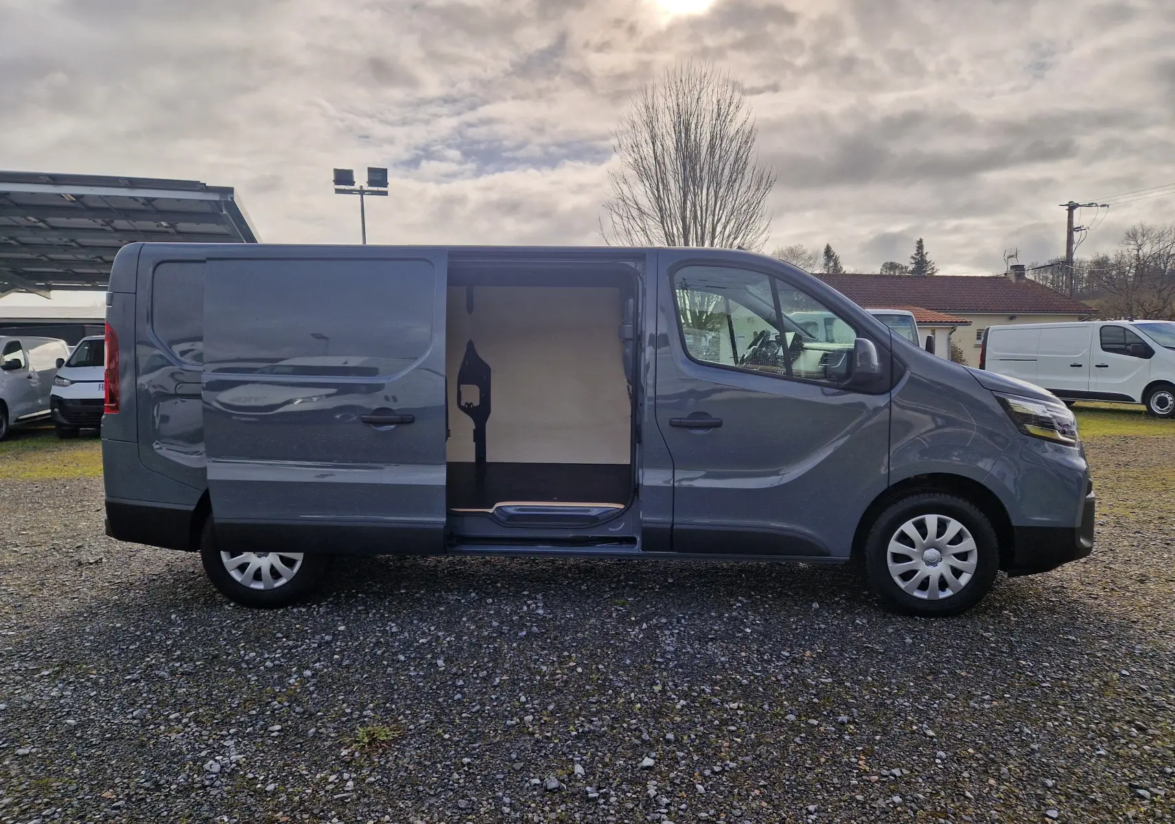 Vue latérale droite d’un Nissan Primastar gris urbain 2025 avec porte coulissante ouverte dévoilant l’espace de chargement.