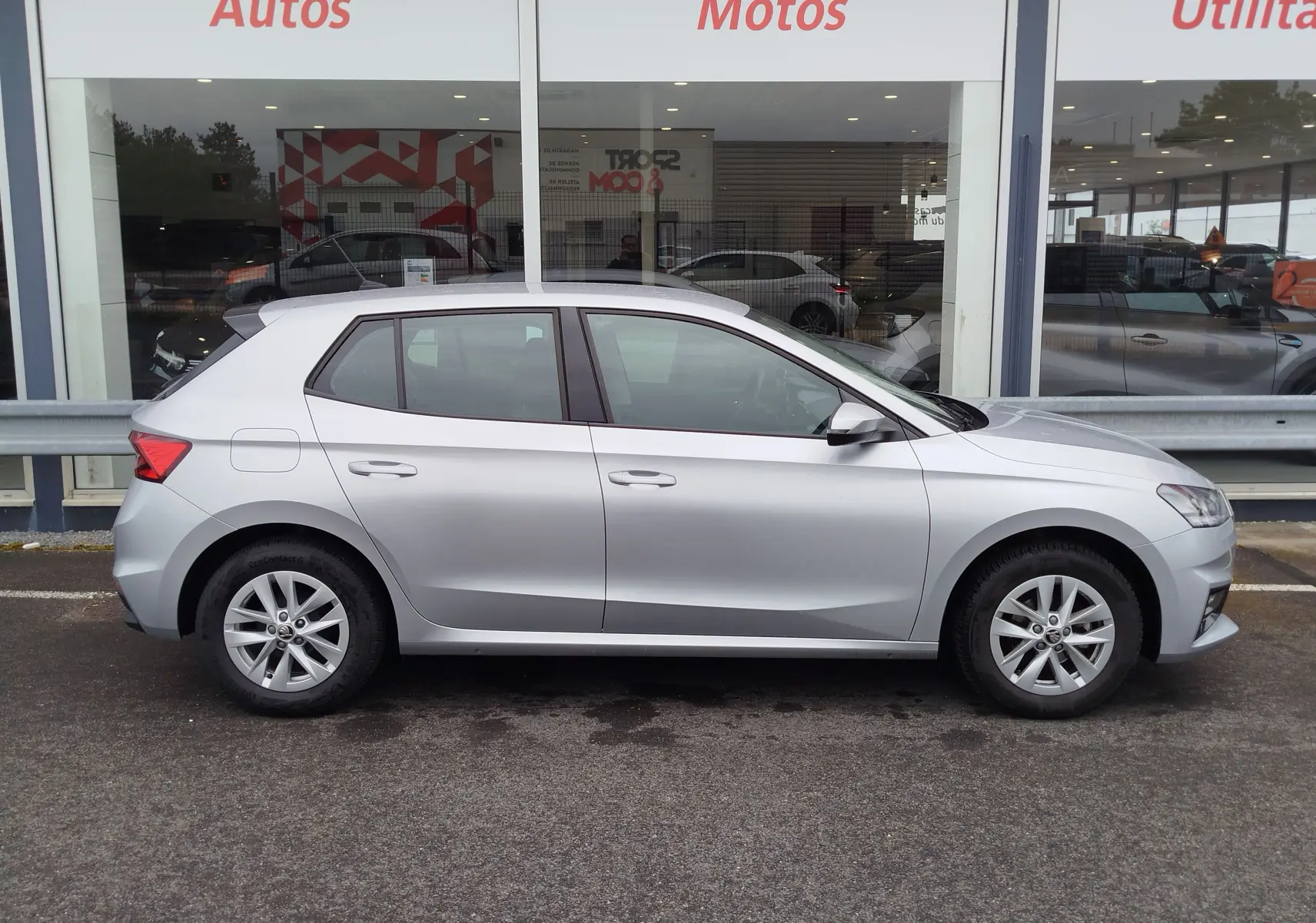 Vue de profil côté gauche d'une Skoda Fabia gris argent métallisé stationnée devant une vitrine de concession.