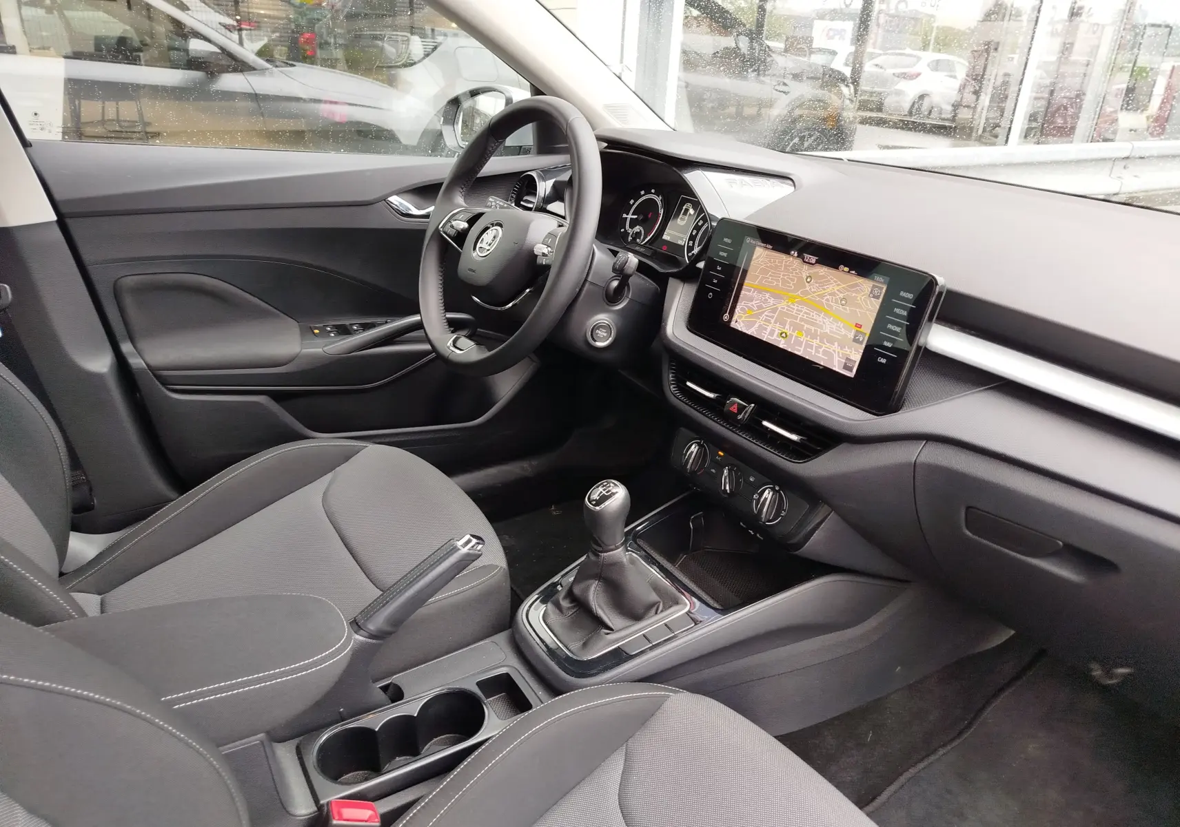 Vue intérieure côté conducteur de la Skoda Fabia 2023, tableau de bord noir avec écran tactile et levier de vitesses manuel.