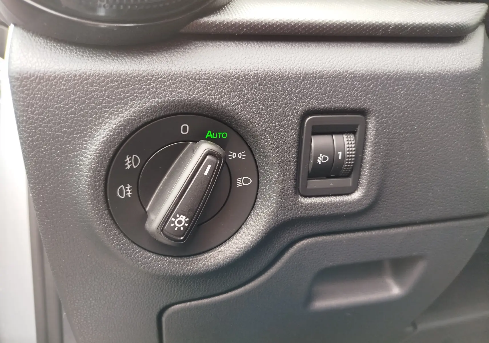Gros plan sur le bouton de commande des phares avec réglage automatique, intérieur noir texturé de la Skoda Fabia gris argent 2023.