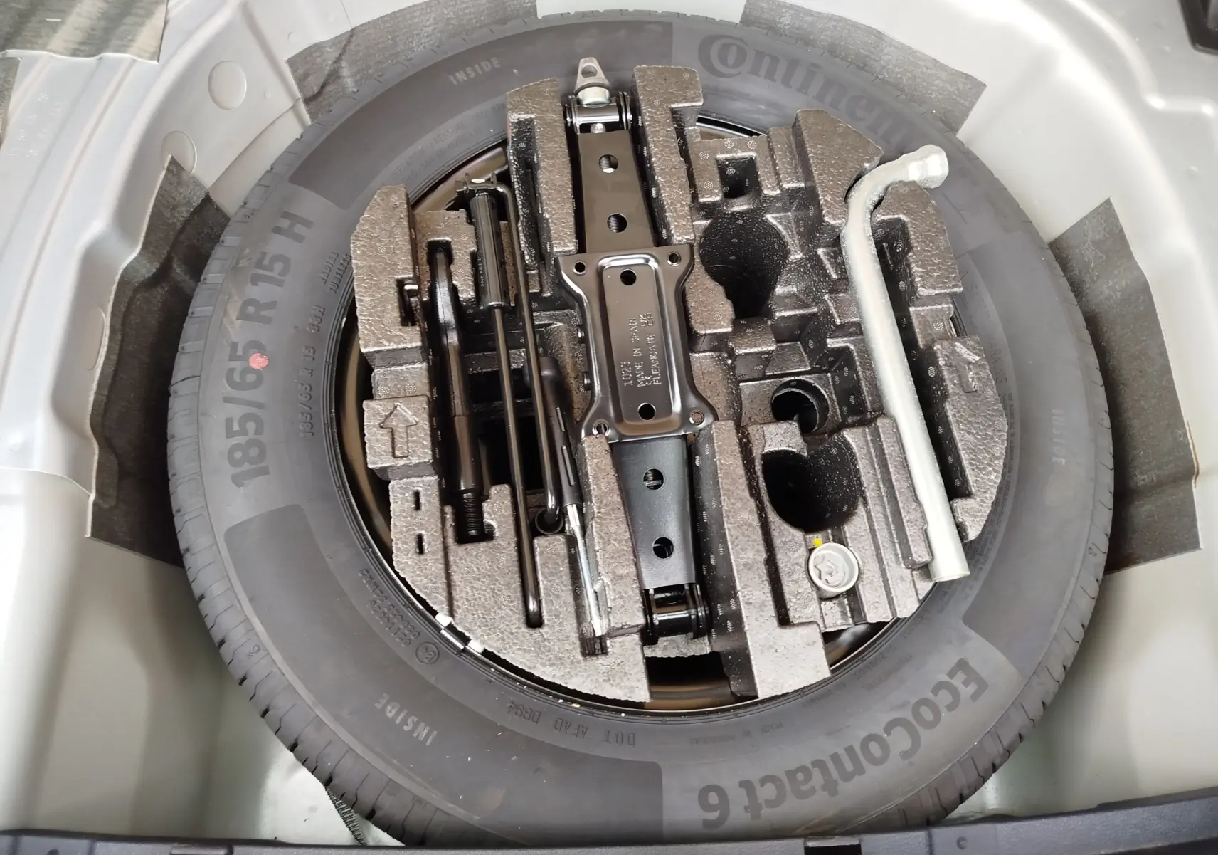 Vue plongeante sur la roue de secours et le kit de réparation logés dans le coffre d'une Skoda Fabia gris argent métallisé 2023.
