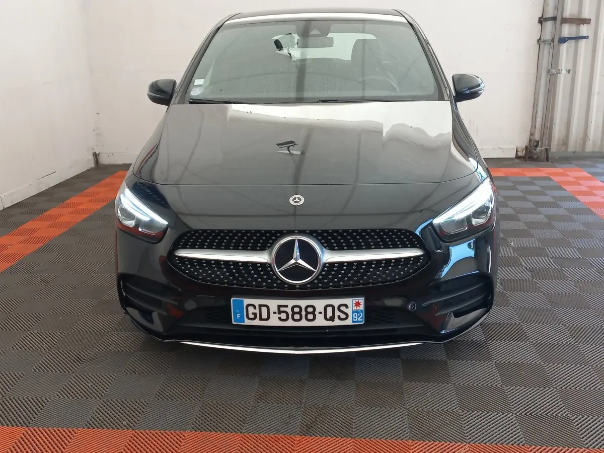 Vue avant d'une Mercedes Classe A Berline A 200 AMG Line noire avec calandre à étoile et phares LED allumés.