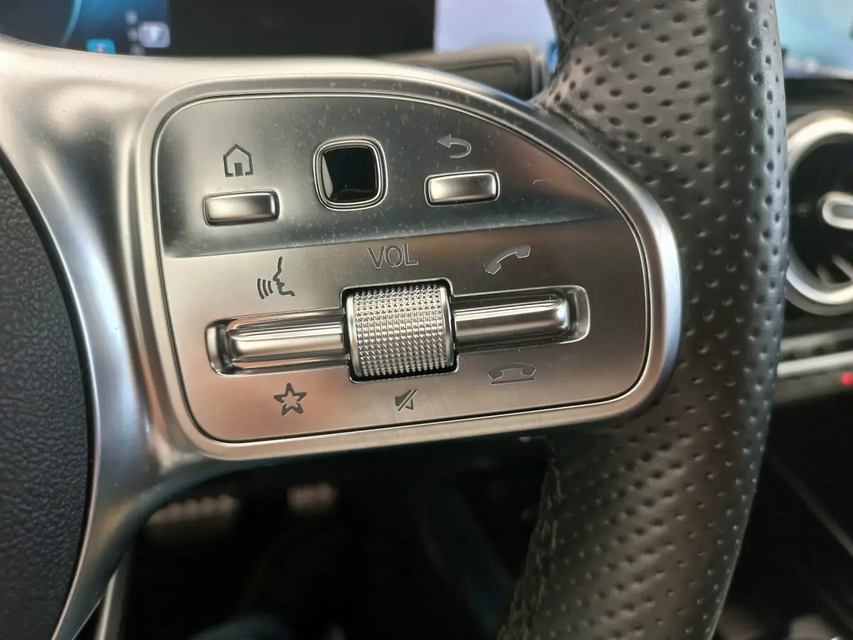 Gros plan sur les commandes argentées du volant en cuir perforé d’une Mercedes Classe A A 200 AMG Line noire.