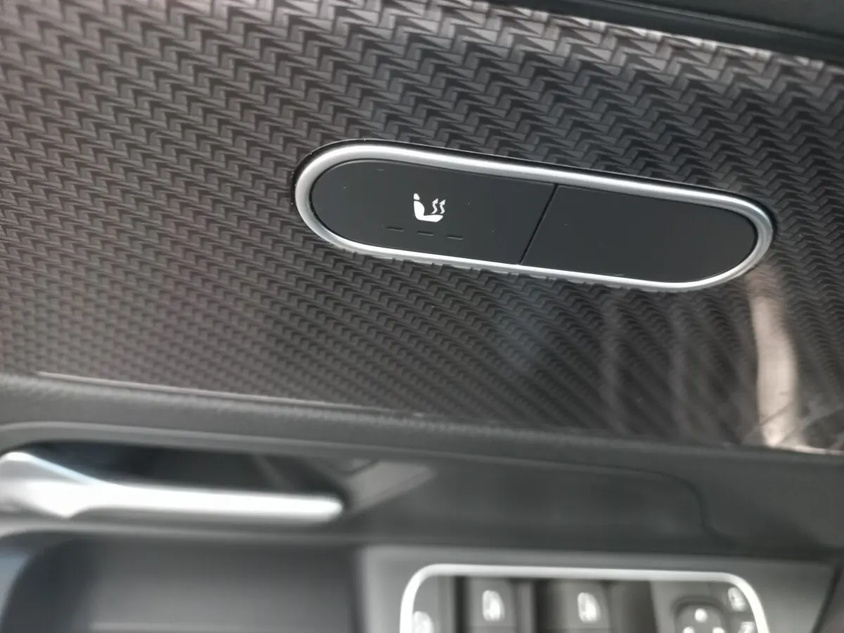 Détail du bouton de chauffage de siège sur la porte intérieure en finition carbone d’une Mercedes Classe A AMG Line noire.