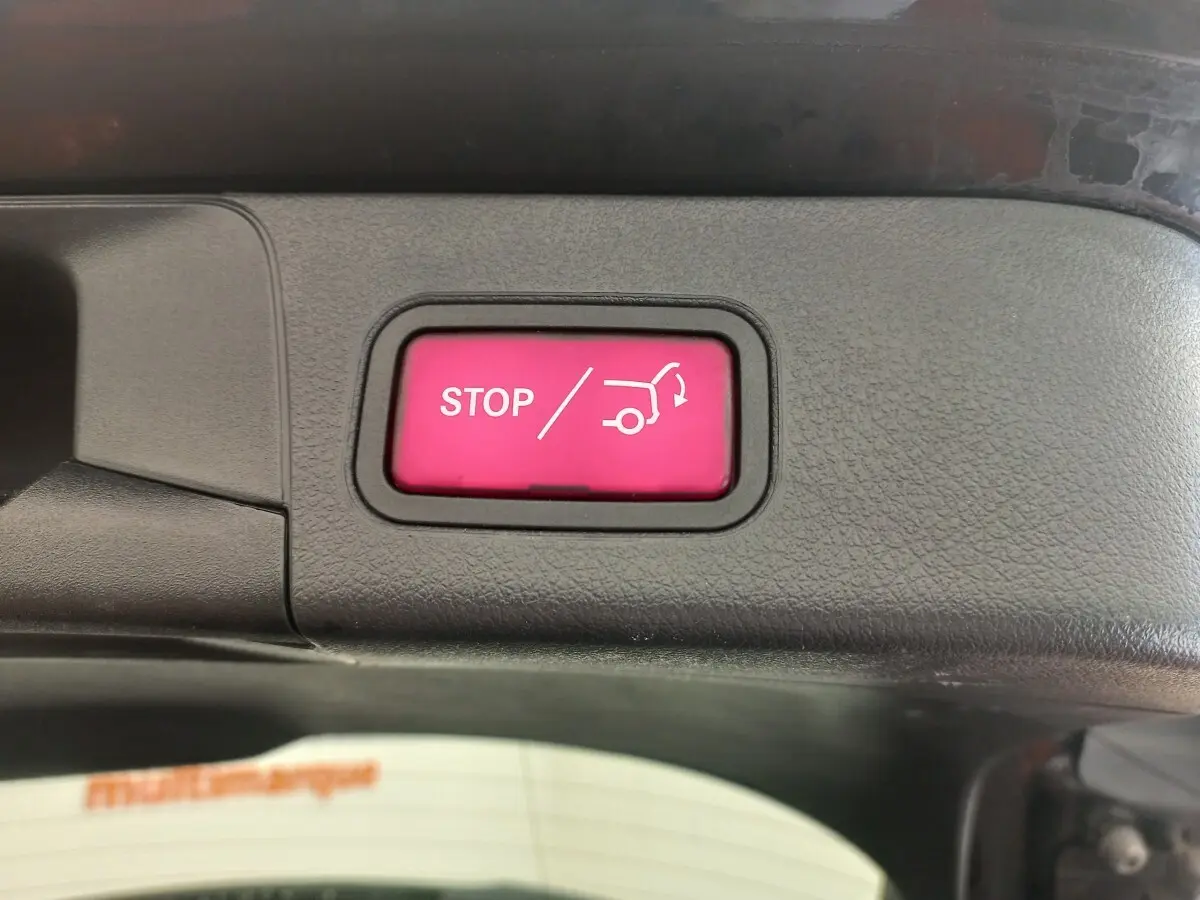 Bouton rouge STOP ouverture/fermeture coffre sur panneau intérieur noir d’une Mercedes Classe A berline noire.
