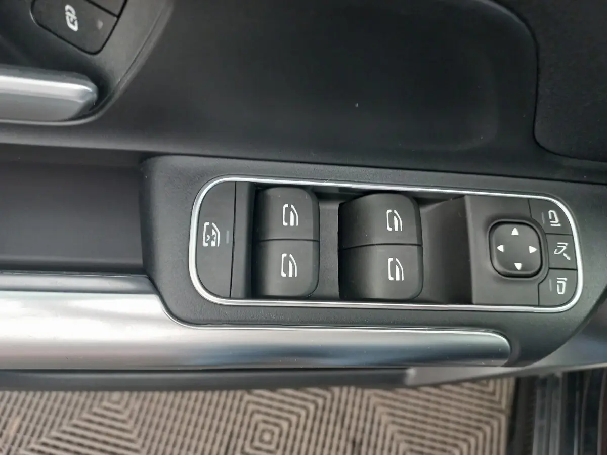 Gros plan sur les commandes des vitres et rétroviseurs côté conducteur d'une Mercedes Classe A berline noire.