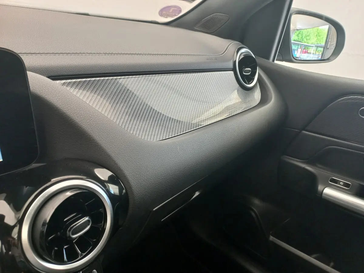 Vue intérieure côté passager de la planche de bord noire avec insert décoratif gris et aérateurs ronds chromés d'une Mercedes Classe A AMG Line.