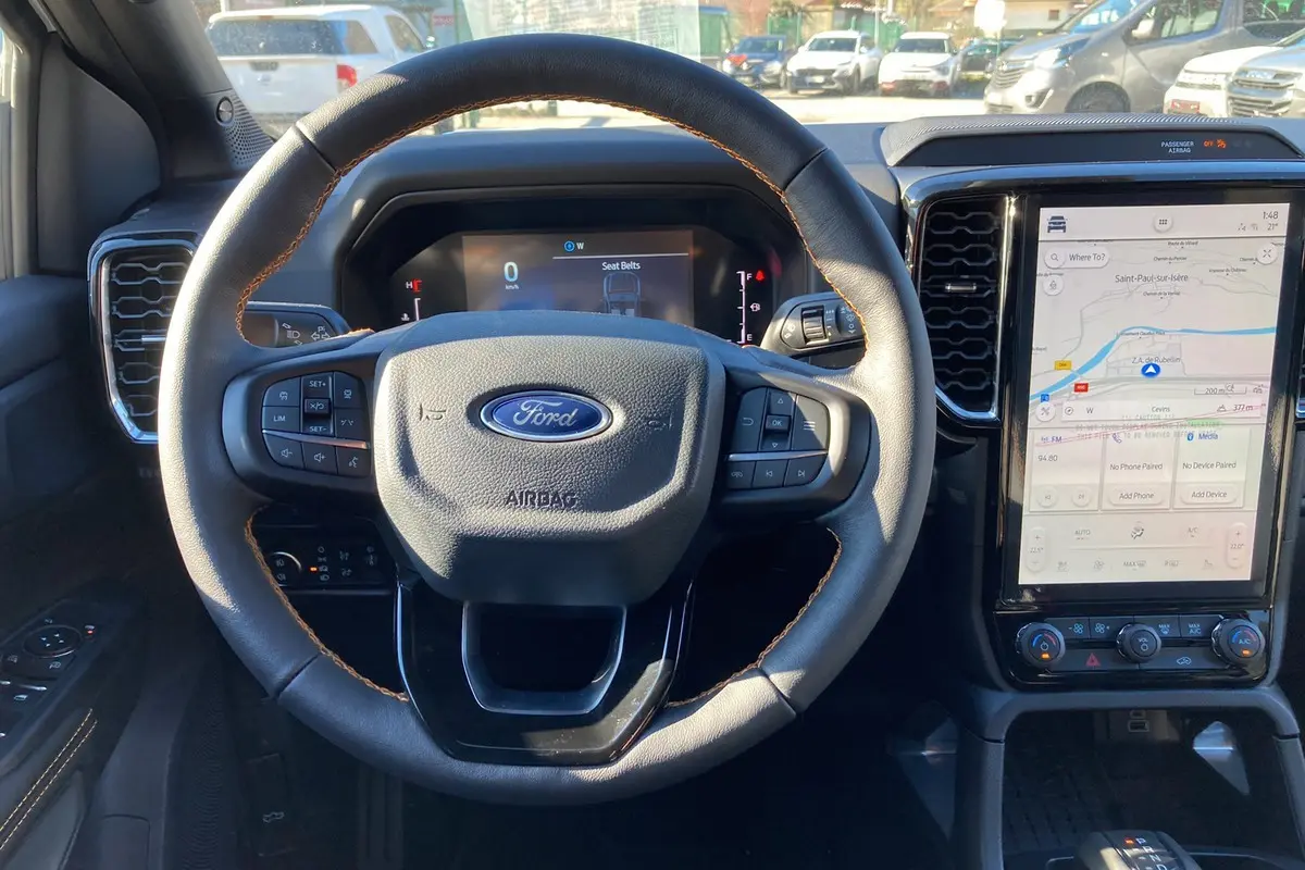 Vue intérieure centrée sur le volant cuir noir avec surpiqûres marron du Ford Ranger 2025 et écran tactile vertical.