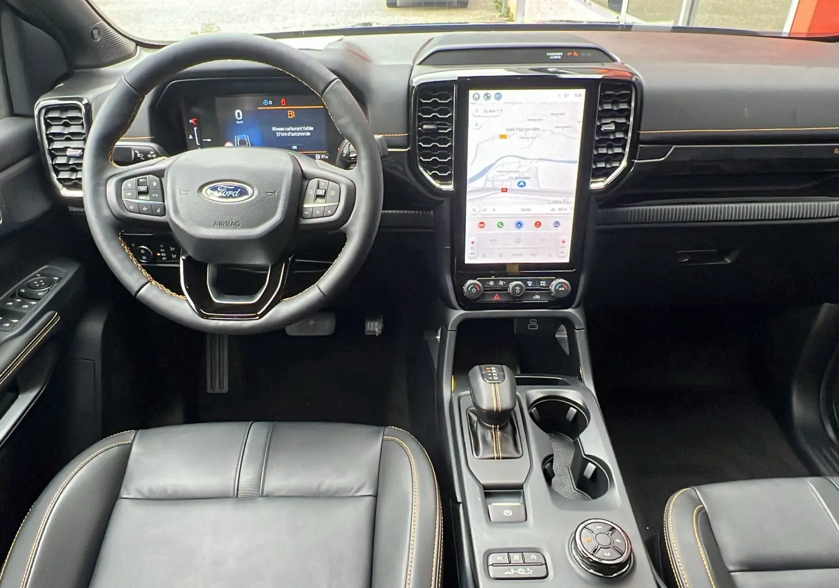 Vue intérieure avant du Ford Ranger 2025 Wildtrak Plus noir agate, avec volant multifonction, écran tactile vertical et coutures orange.