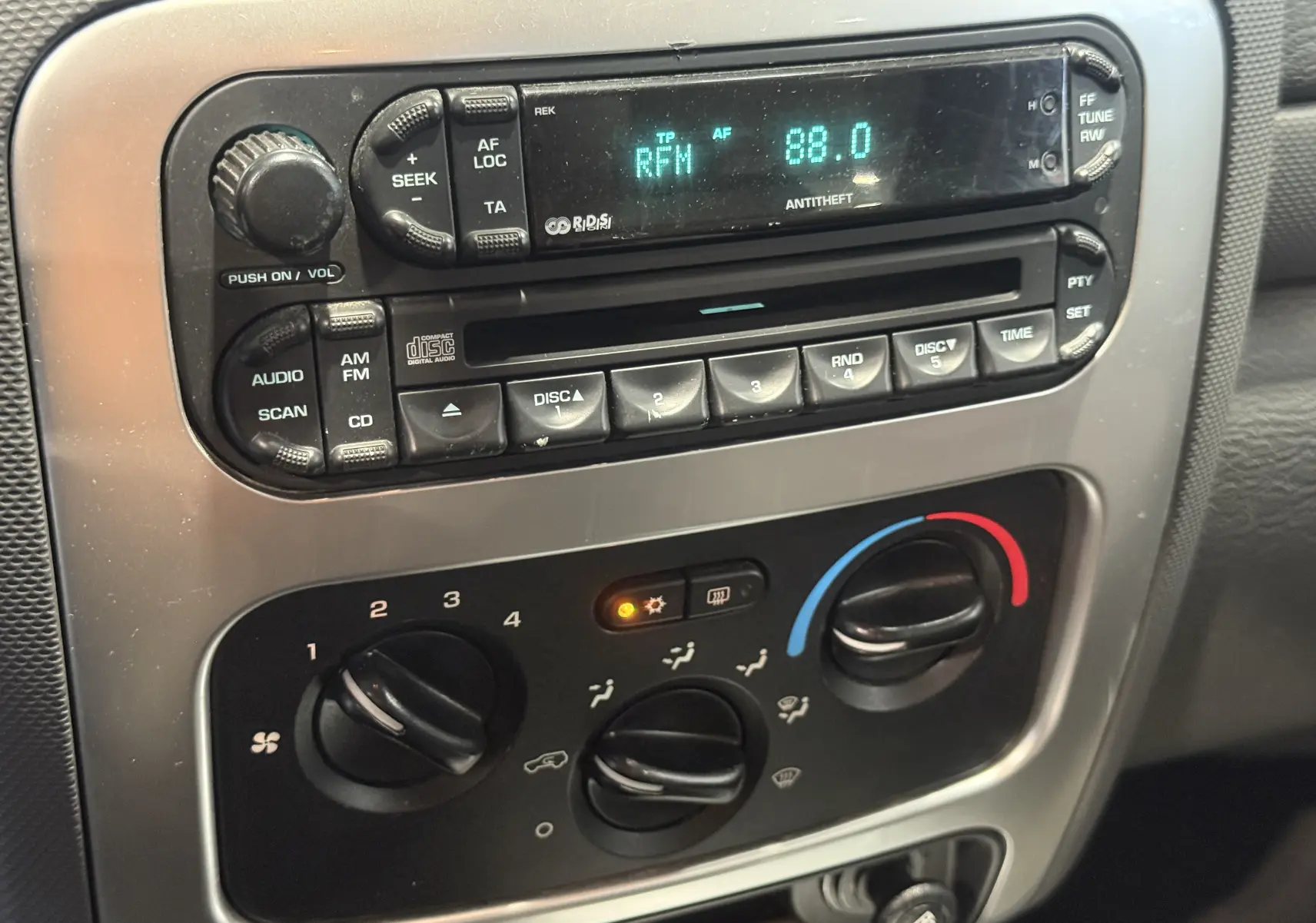 Gros plan sur la console centrale du Jeep Cherokee bleu 2005, montrant la radio et les commandes de climatisation.