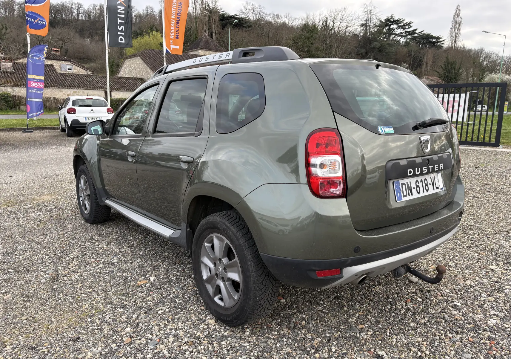 Vue 3/4 arrière droite d'un Dacia Duster vert foncé de 2014 avec attelage et barres de toit visibles.