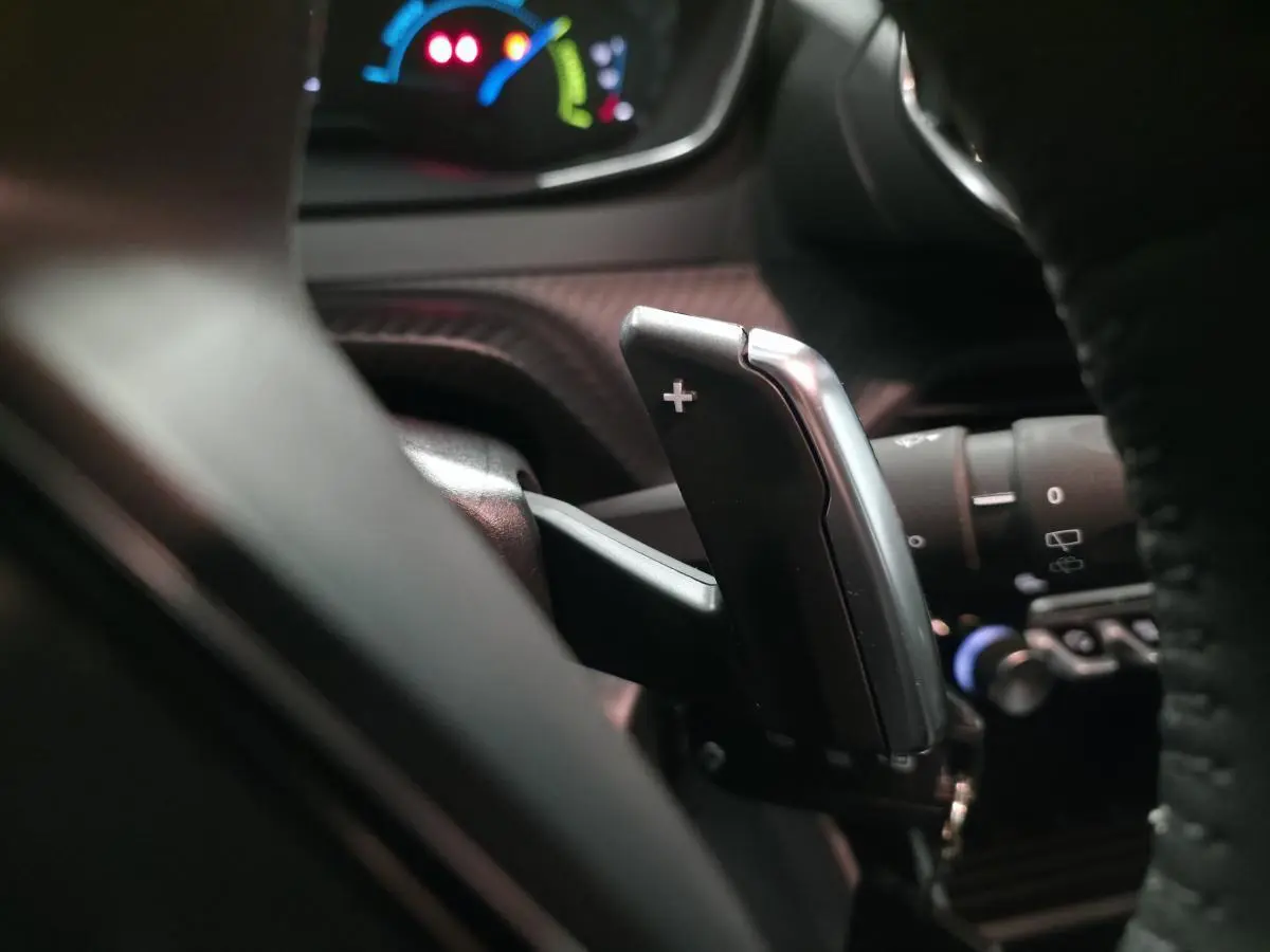 Gros plan sur la palette de changement de vitesse + au volant cuir noir du Peugeot 2008 gris hybride 2025.