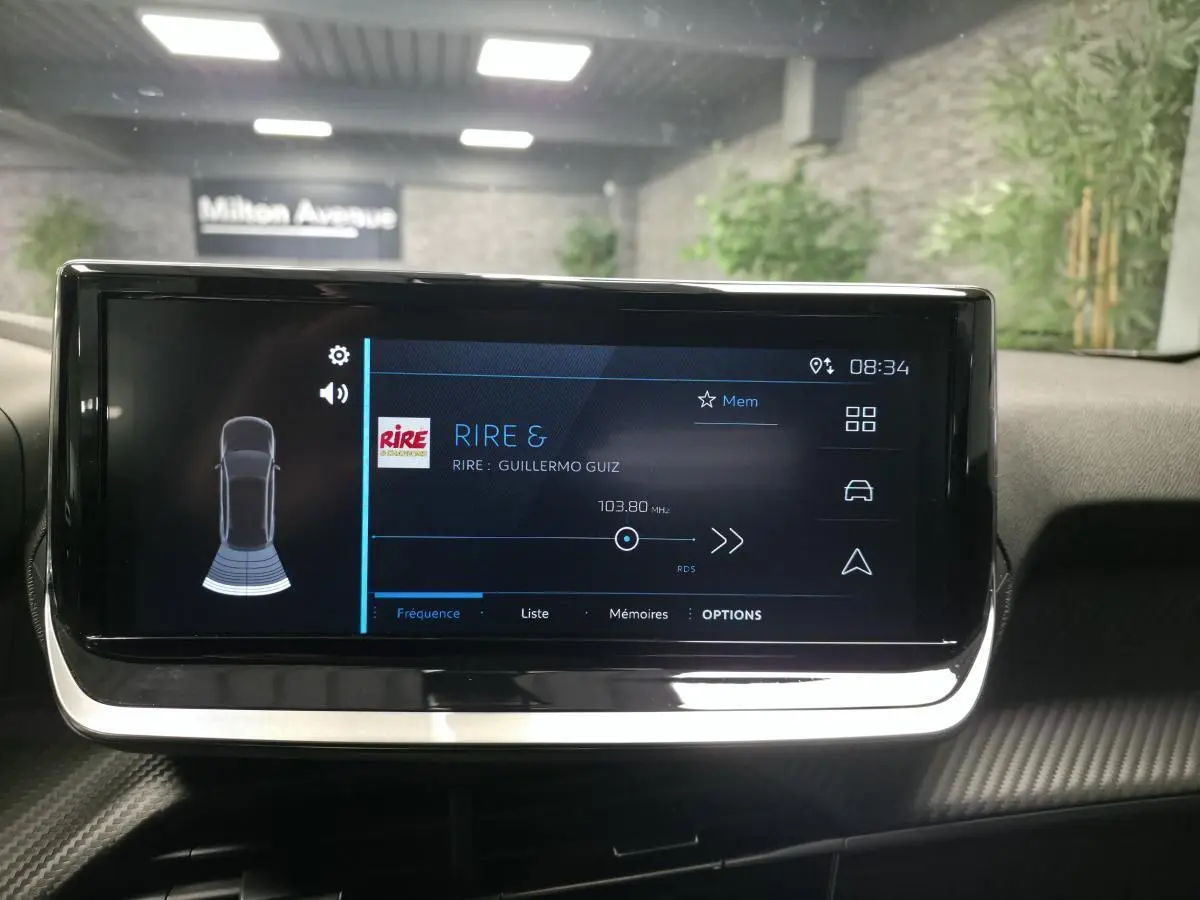 Écran tactile central du Peugeot 2008 gris, affichant la radio et l'aide au stationnement arrière.