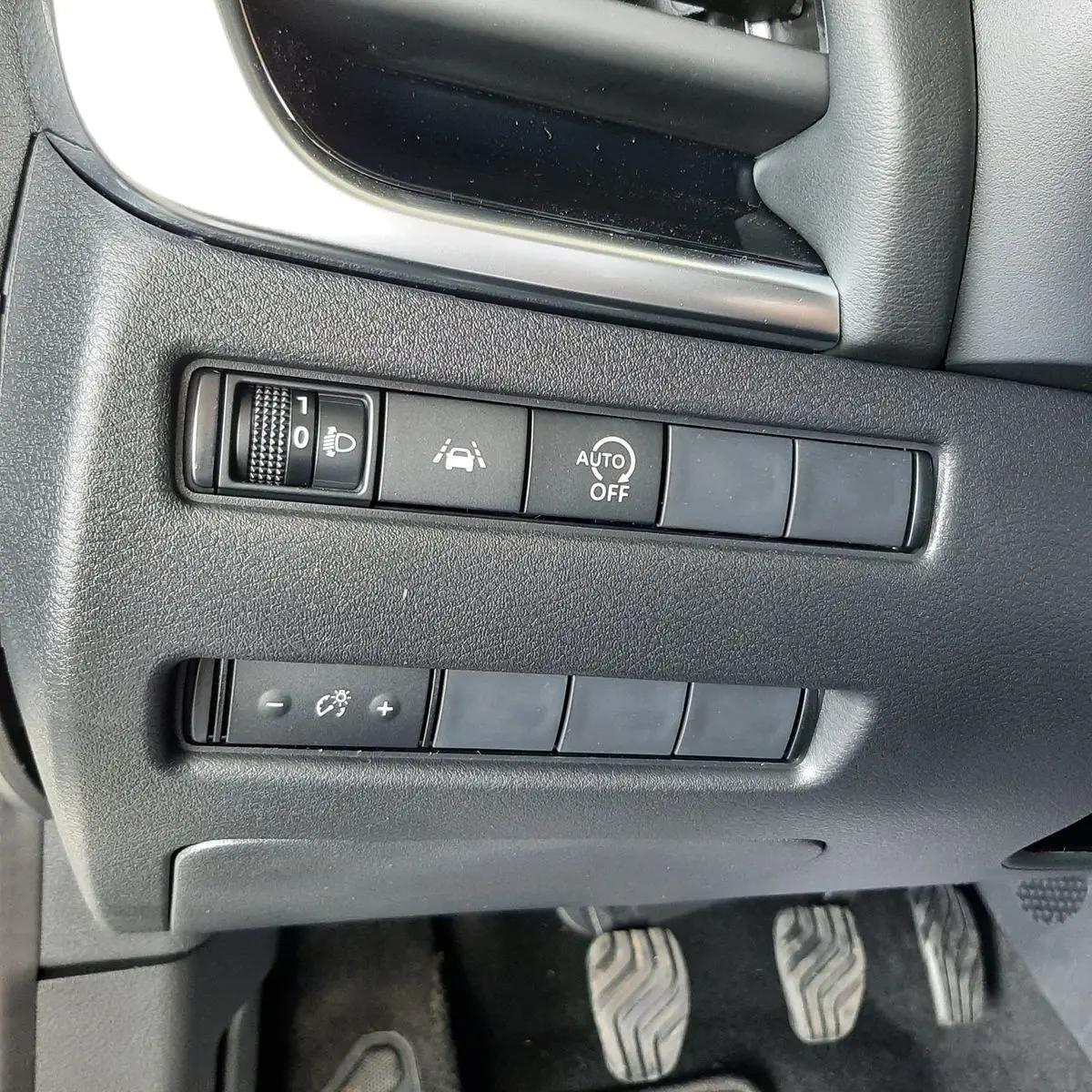 Vue rapprochée des commandes de réglage d'éclairage et d'assistance sur la gauche du tableau de bord d'un Nissan Qashqai blanc lunaire 2022.