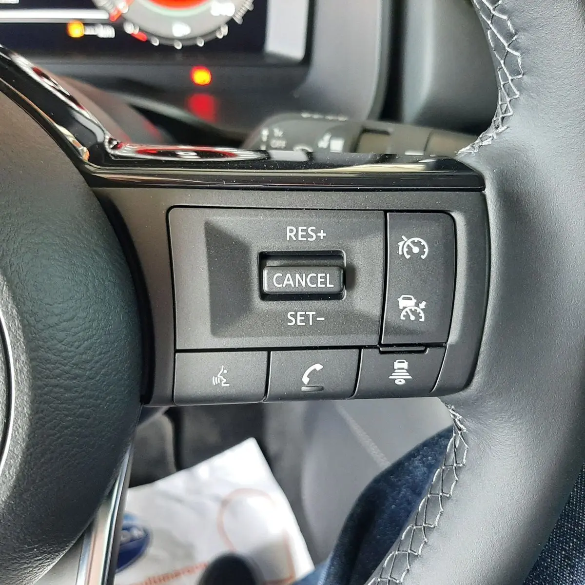 Gros plan sur les commandes de régulateur de vitesse au volant cuir noir du Nissan Qashqai blanc lunaire 2022.
